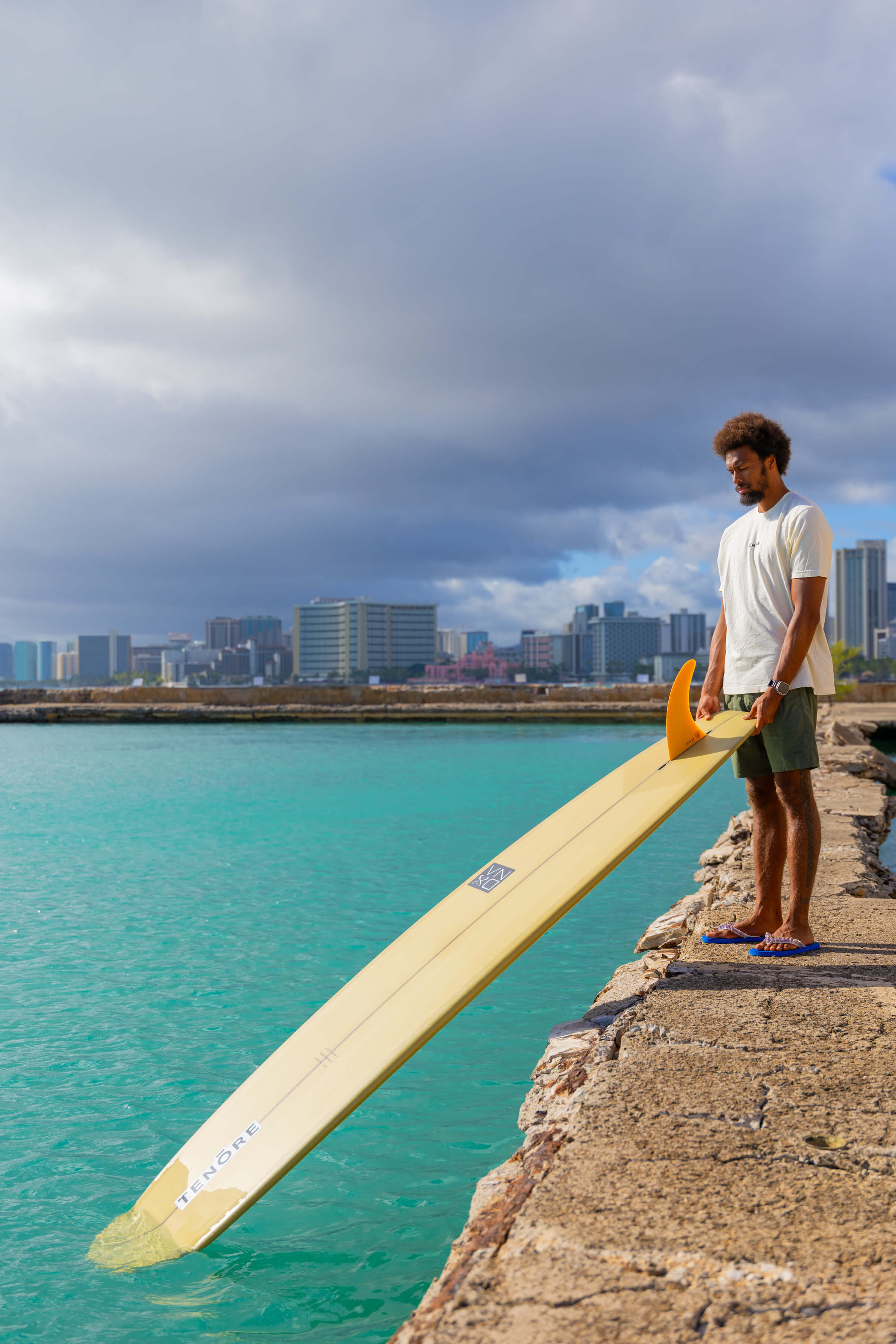 man holding yellow surfboard dipped into water