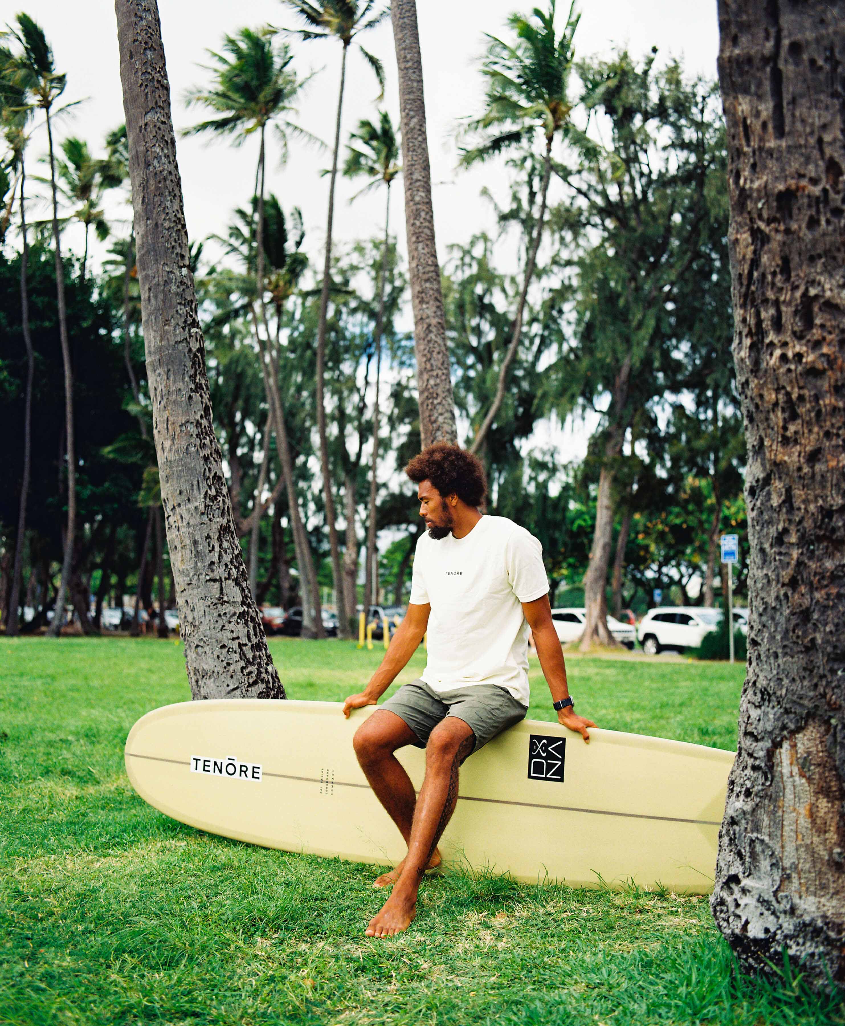 man sitting on yellow surfboard amongst palm trees