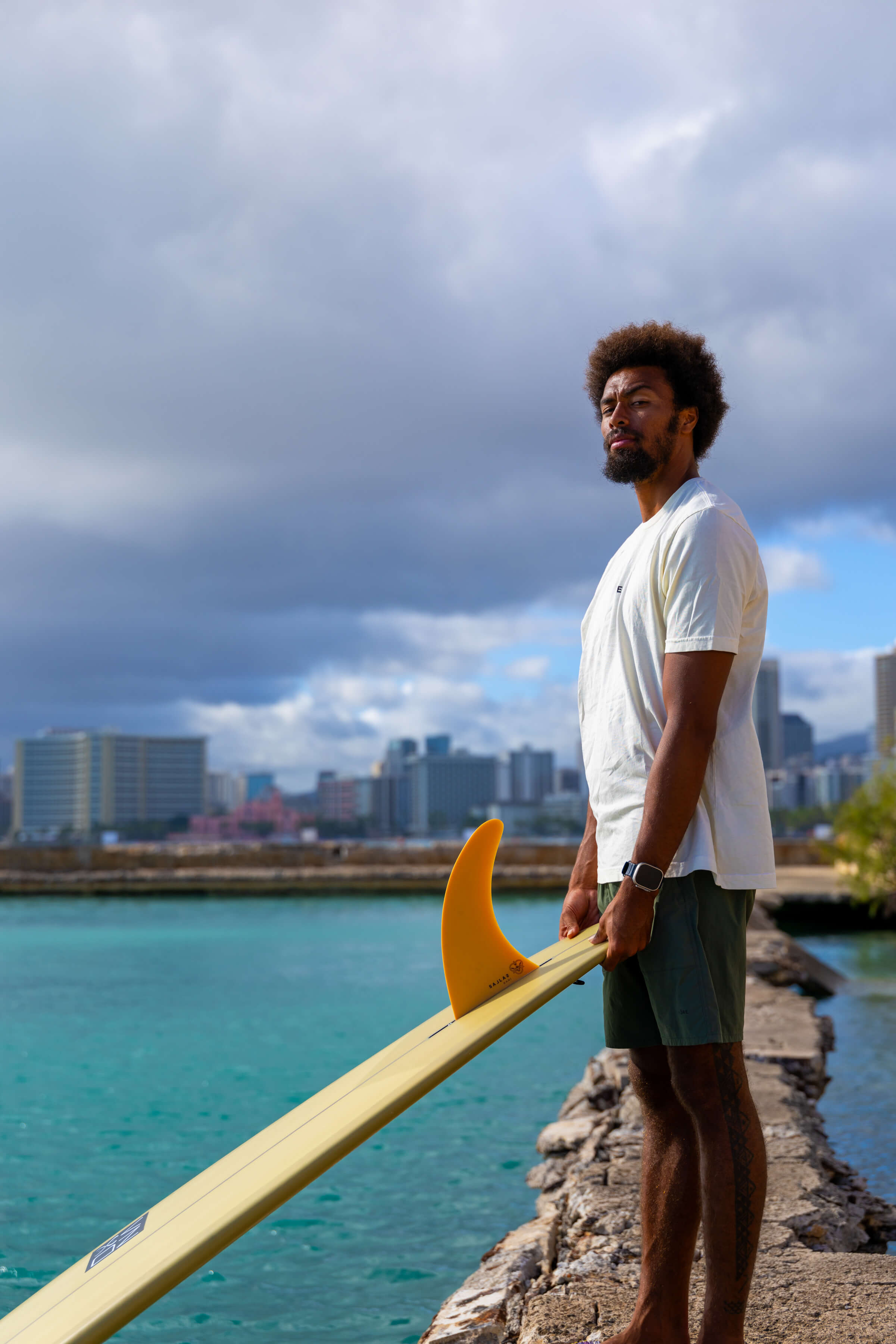 man looking sternly at camera while holding surfboard over dock into water