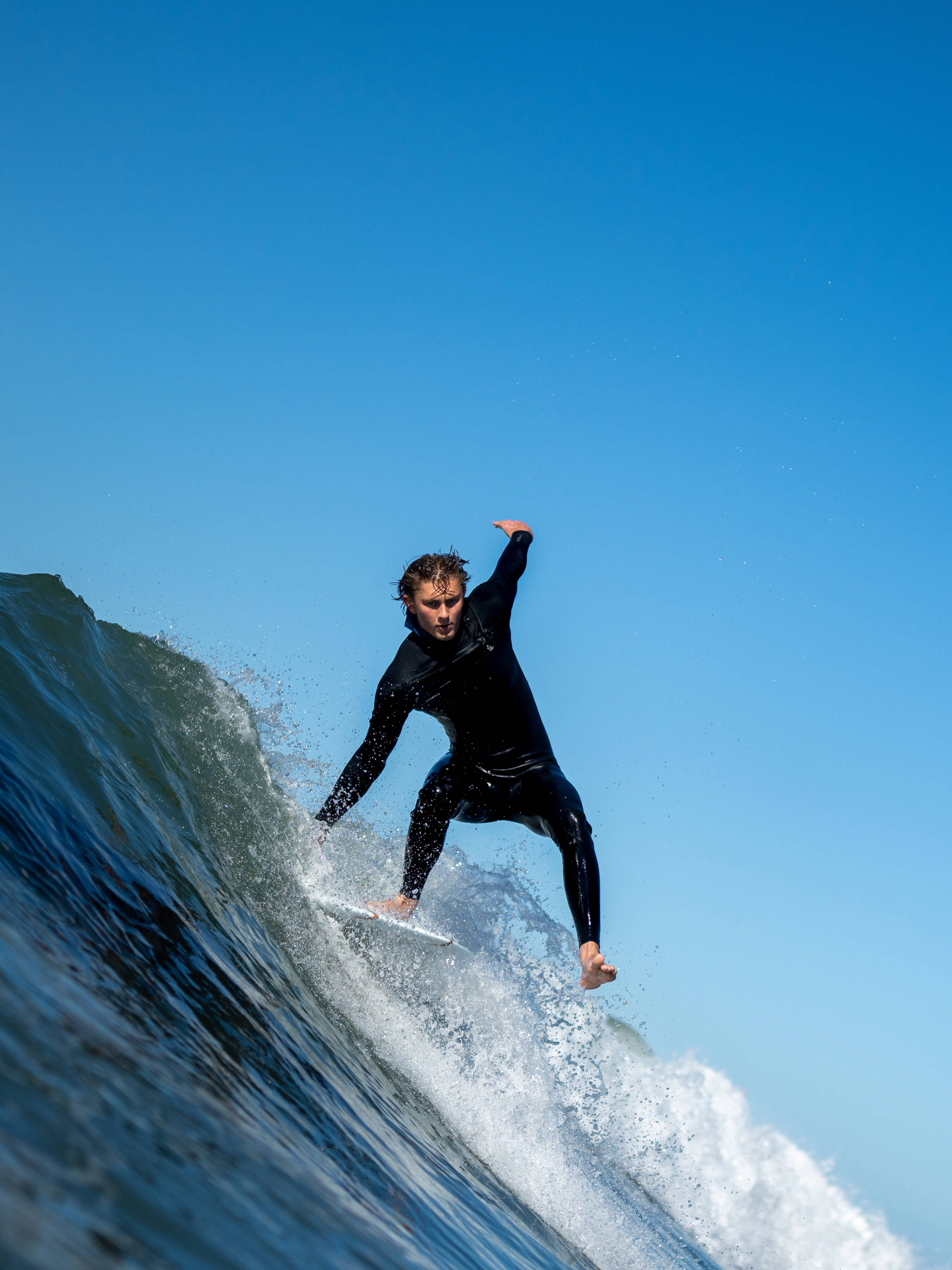 man standing on one foot in black wetsuit riding a wave