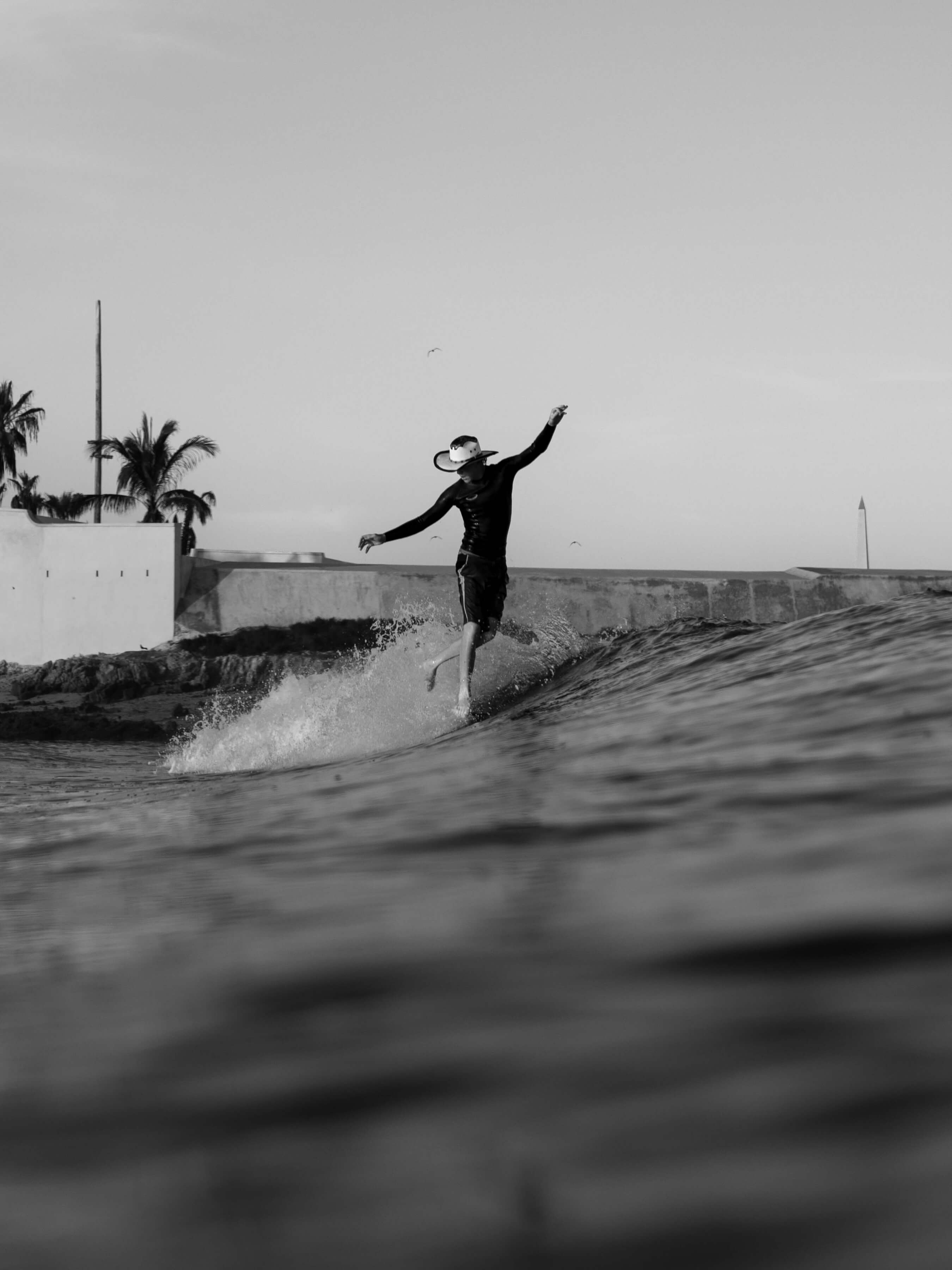 black and white photo of man in cowboy hat on a surfboard