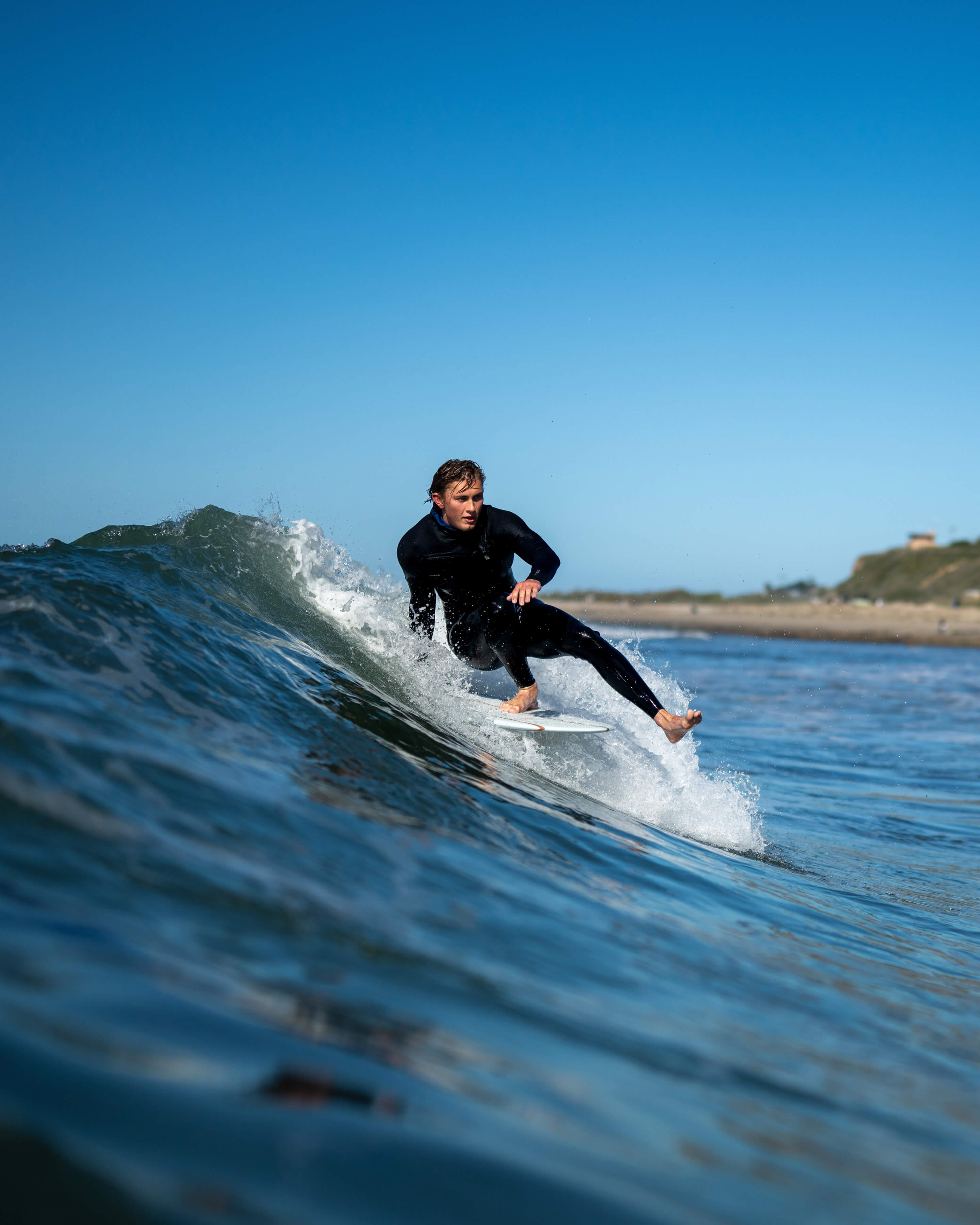 man doing a trick on one foot on surfboard in black wet suit