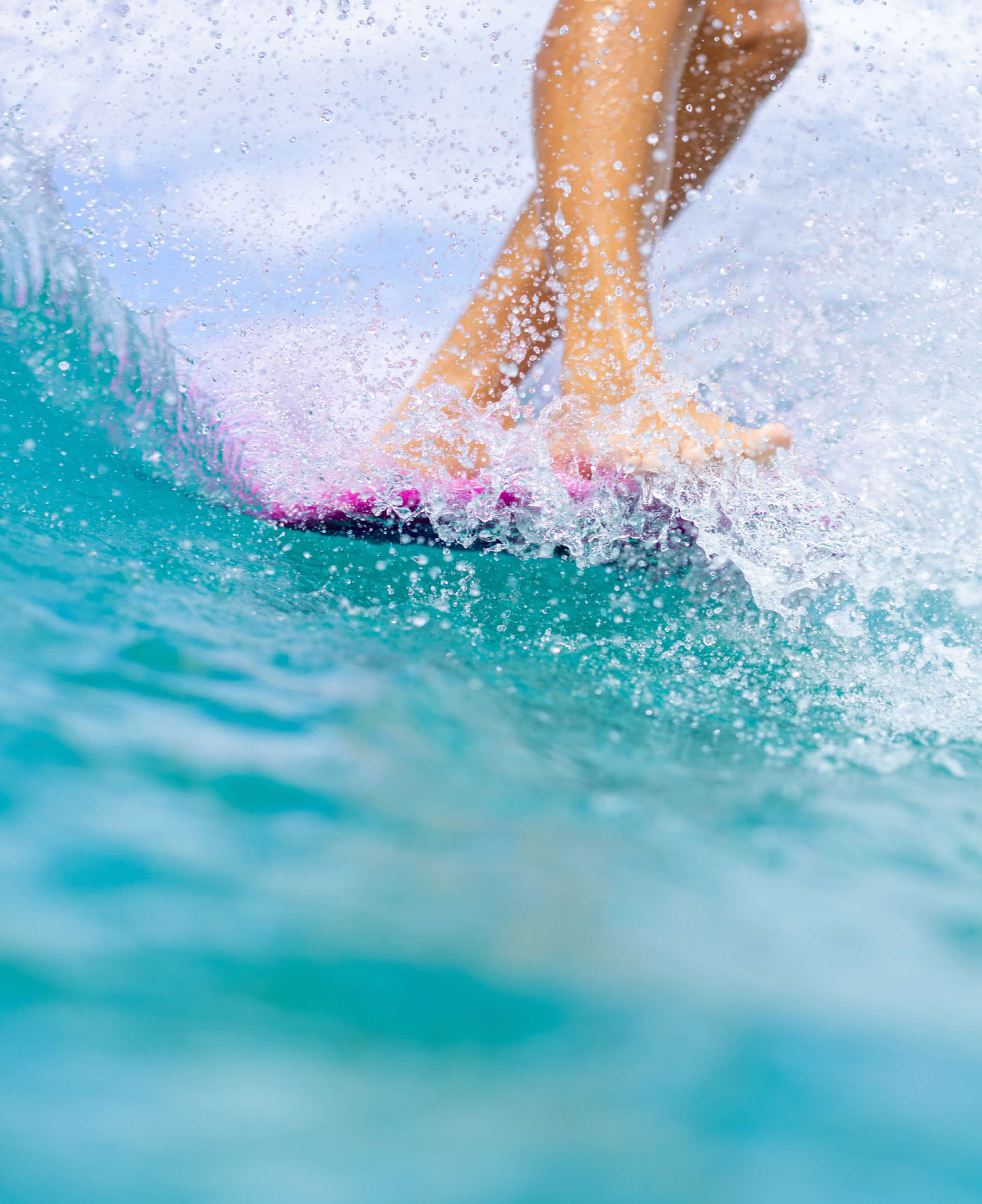 close up of feet on front of pink surfboard with water droplet details