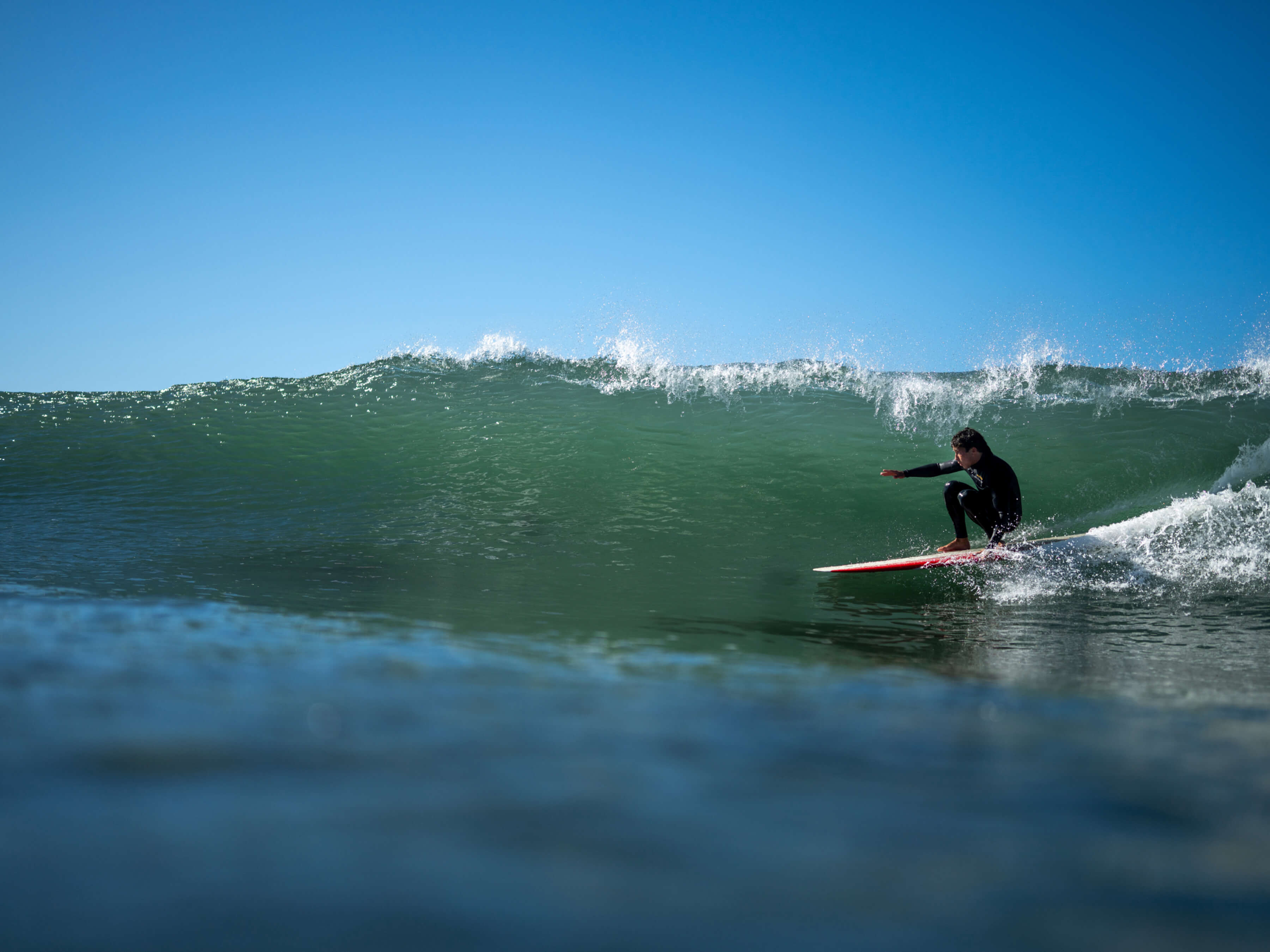 man in black wet suit on surfboard crouching below wave