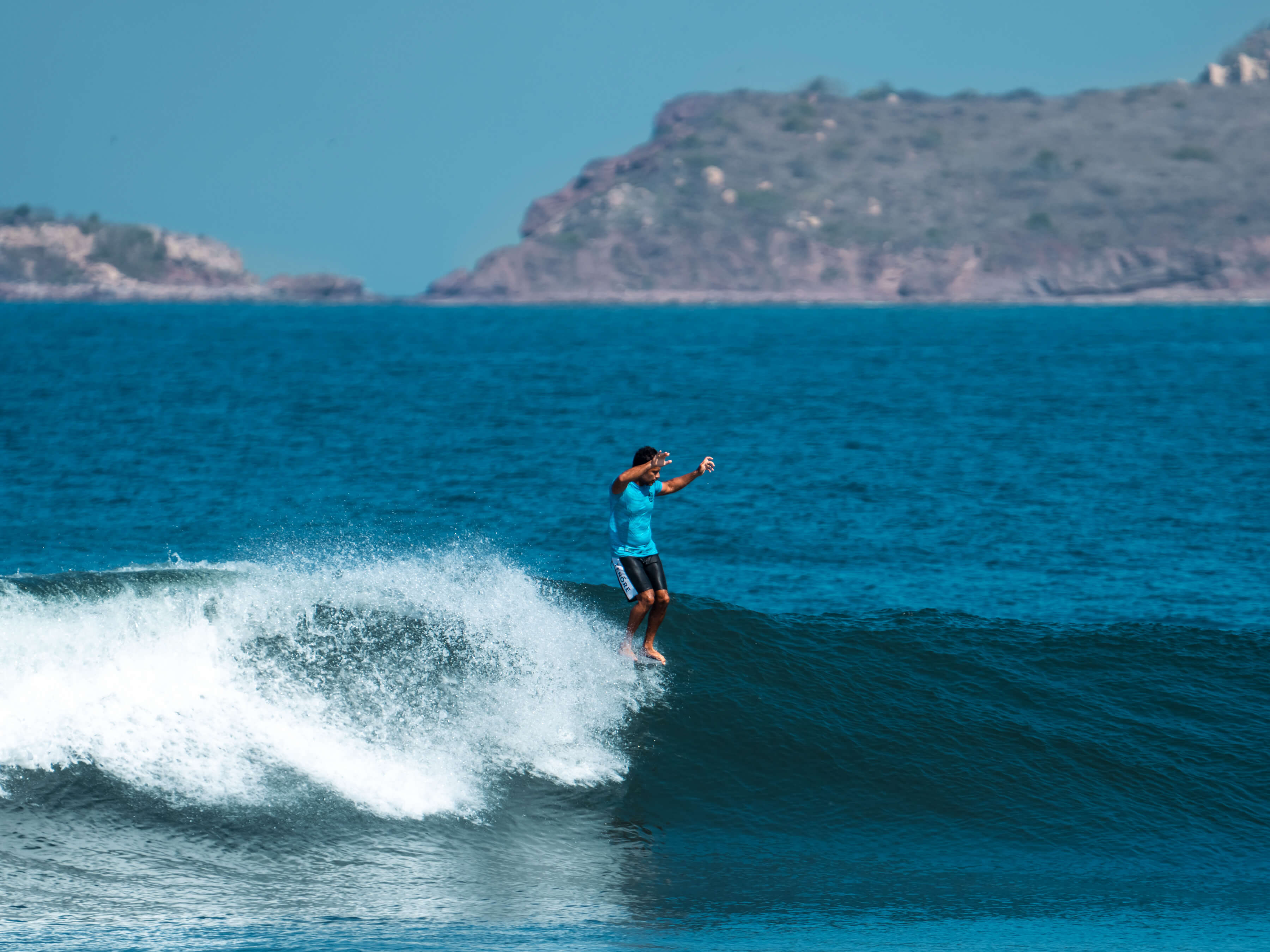 man in blue tshirt and swim trunks riding a wave with ocean background