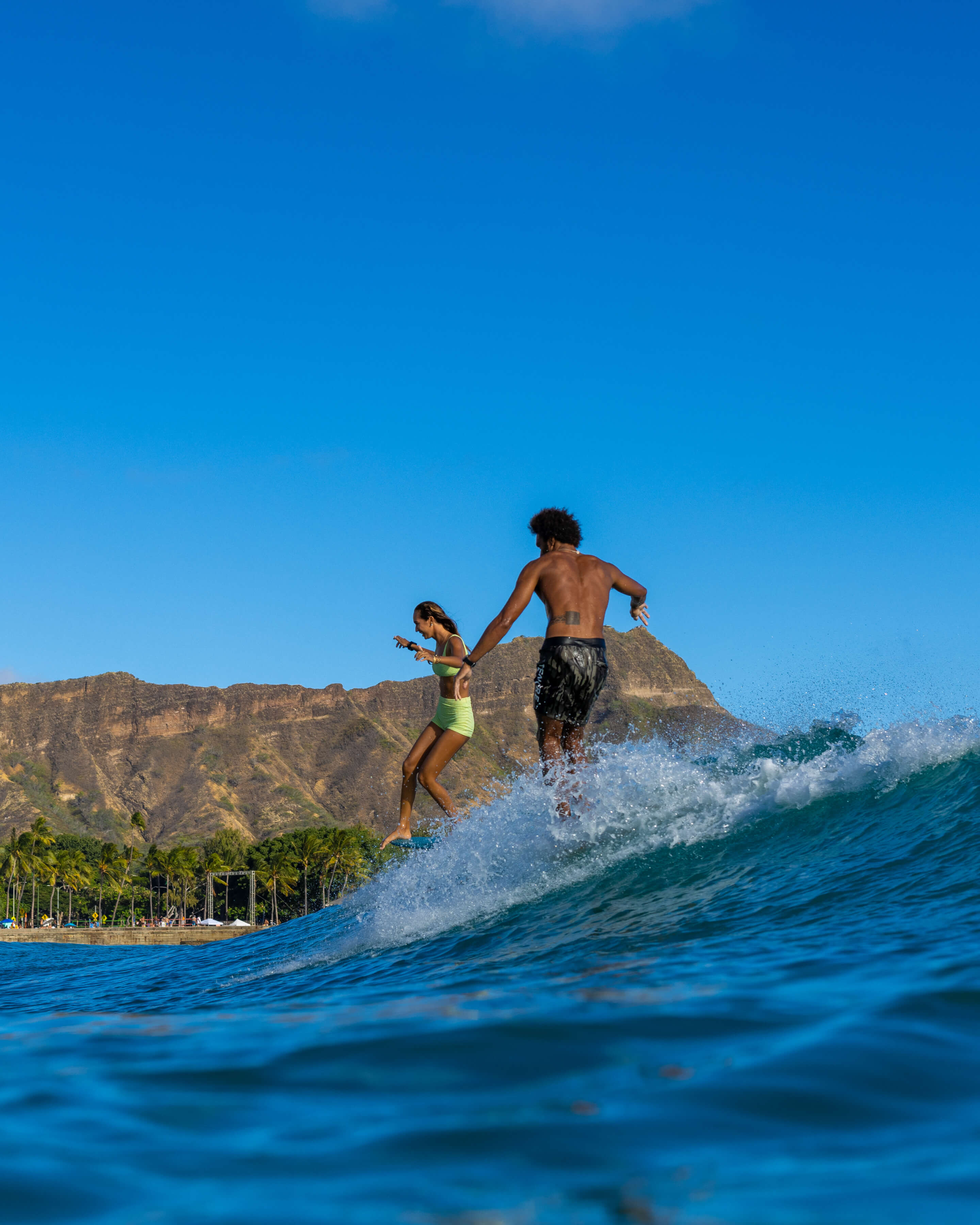 man and woman playing on a wave with hawaiian mountains in background