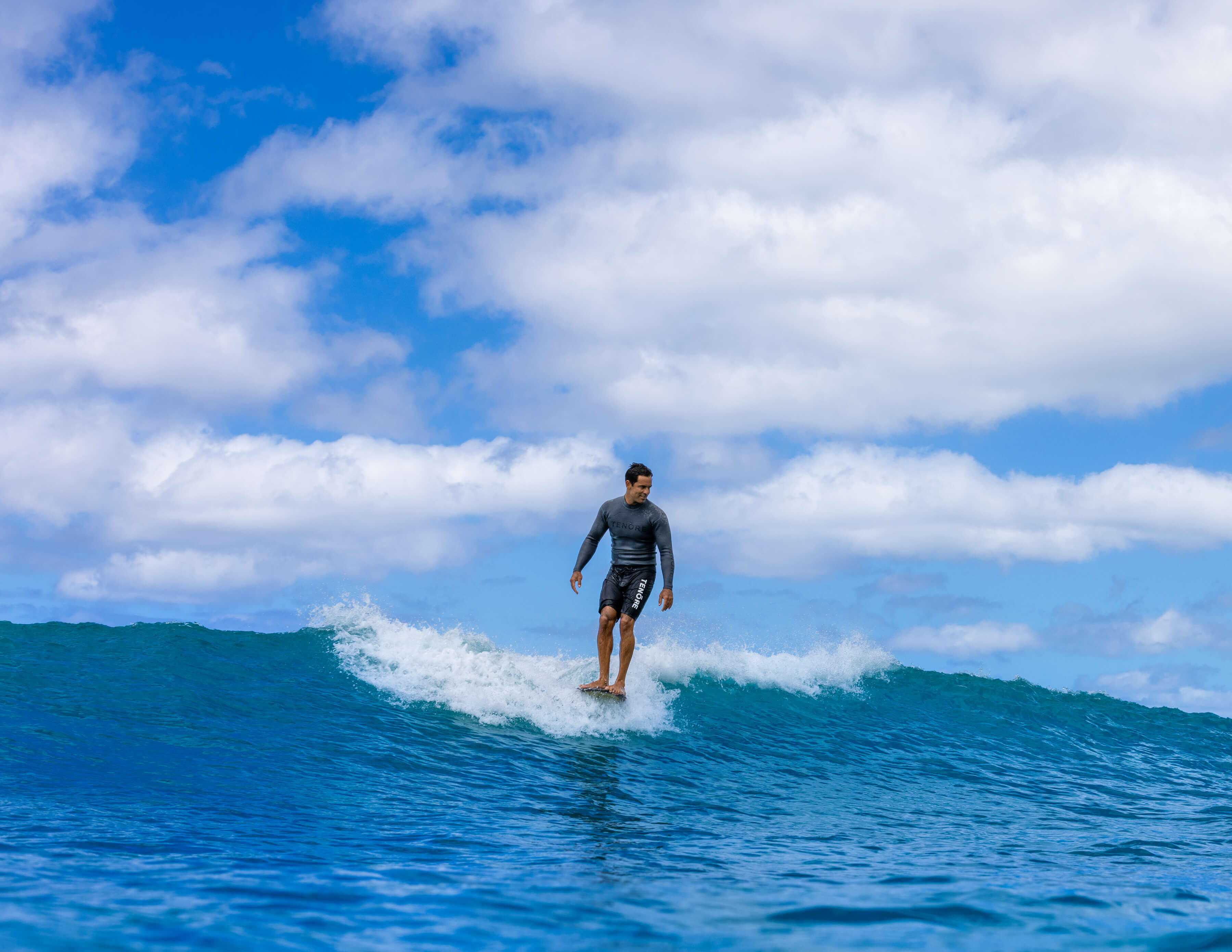 man in black swim trunks riding a wave and smiling