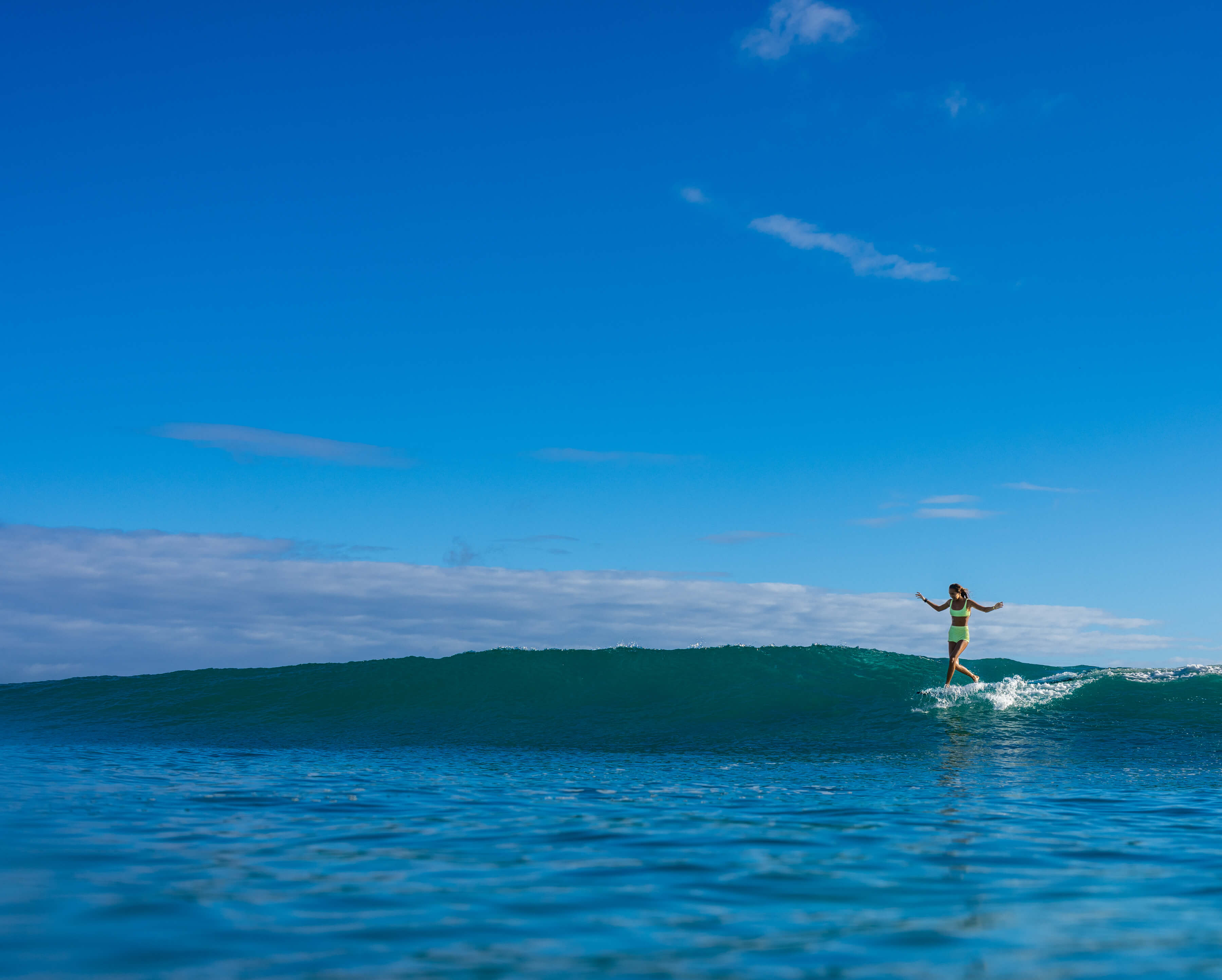 far out view of woman dancing on surfboard while riding a wave